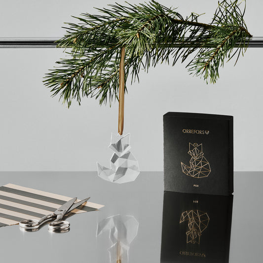 Orreforss crystal fox ornament hanging from a gold ribbon with a black box featuring a fox design on a reflective surface.