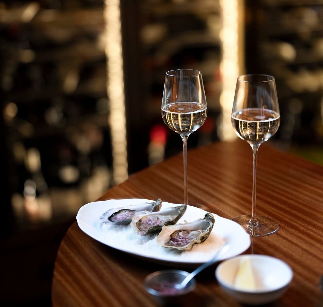 2 long stem champage glasses on a table next to a plate of 3 oysters