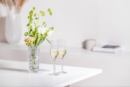 2 champagne glasses on the counter filled with champagne next to a vase filled with green, pink, and white flowers