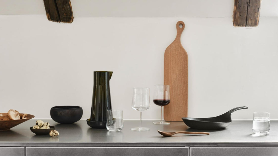 counter top filled with different home pieces, such as glassware, a pan, cutting board, and a wooden spoon