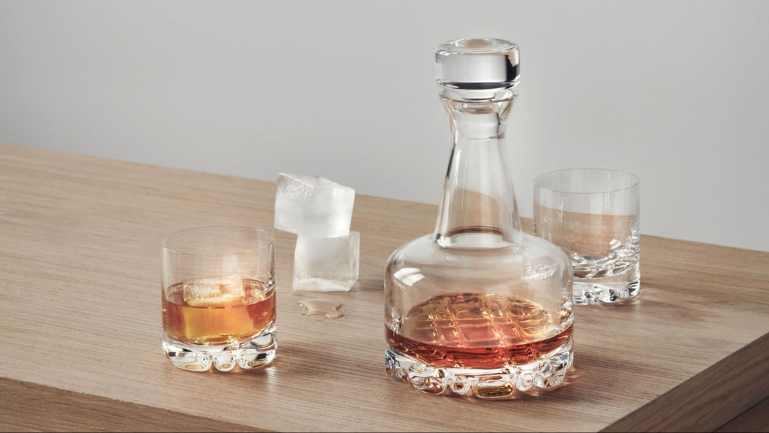 whiskey decanter and 2 whiskey glasses on a wooden table with ice cubes