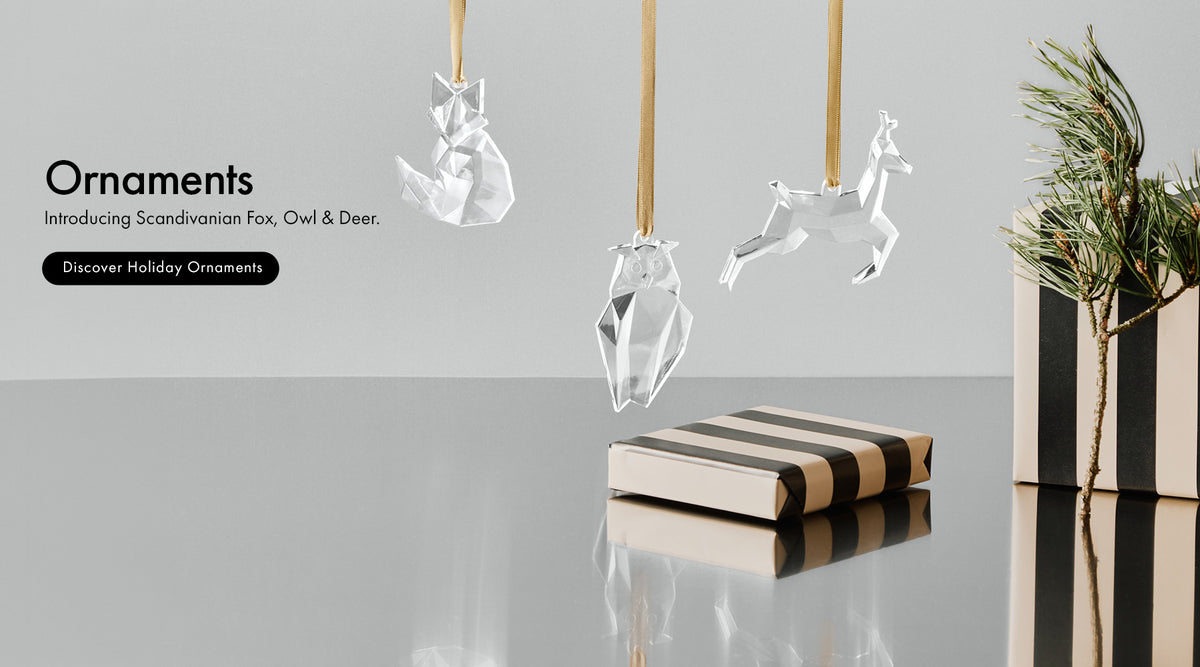 Three transparent hanging holiday ornaments shaped like a fox, owl, and deer are displayed against a light gray background, with a striped gift box and a small plant beside them. Text on the left reads 'Ornaments' and 'Introducing Scandinavian Fox, Owl & Deer.