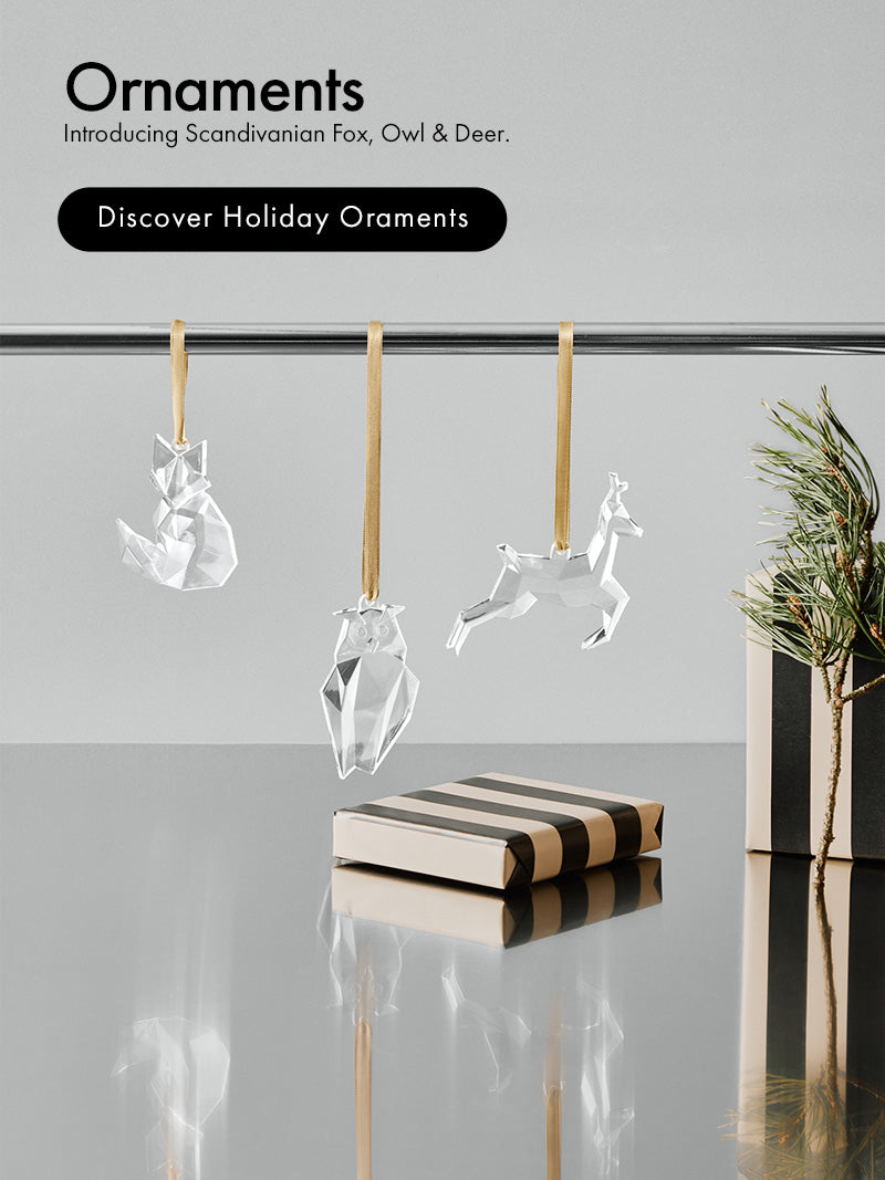Three transparent hanging holiday ornaments shaped like a fox, owl, and deer are displayed against a light gray background, with a striped gift box and a small plant beside them. Text on the left reads 'Ornaments' and 'Introducing Scandinavian Fox, Owl & Deer.