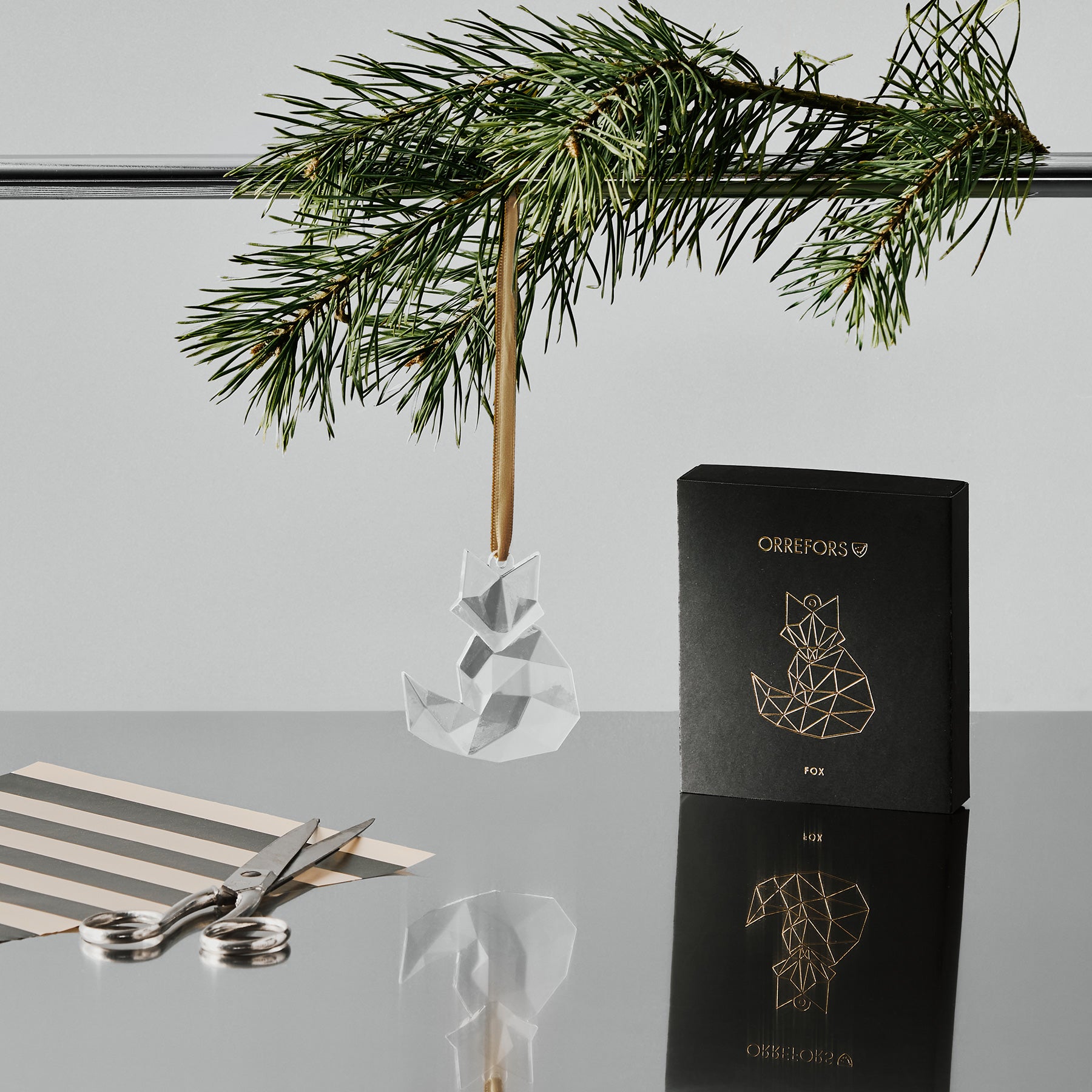 Orreforss crystal fox ornament hanging from a gold ribbon with a black box featuring a fox design on a reflective surface.