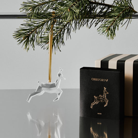 Decorative deer ornament hanging from a rod with a branch next to a black box with gold design on a gray surface.