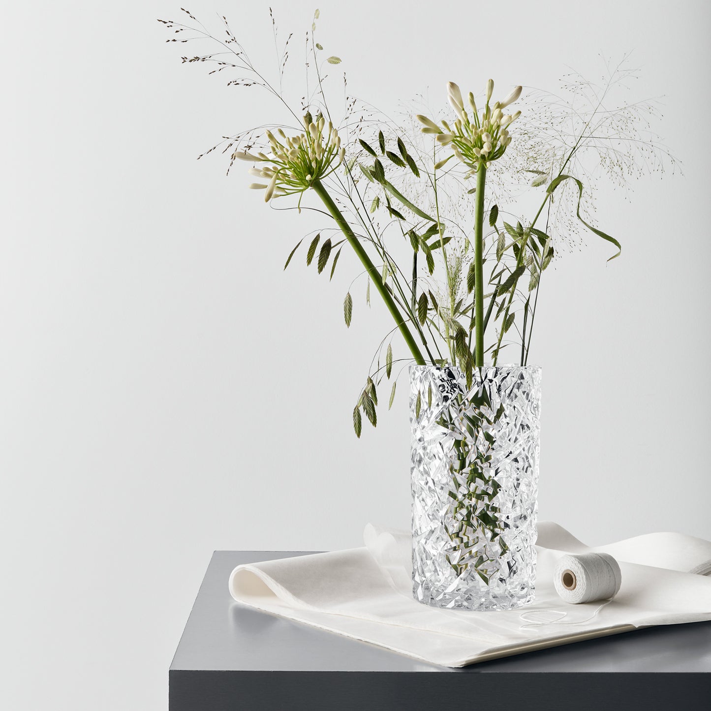 Clear glass vase with decorative pattern containing greenery on a white surface with a light gray background