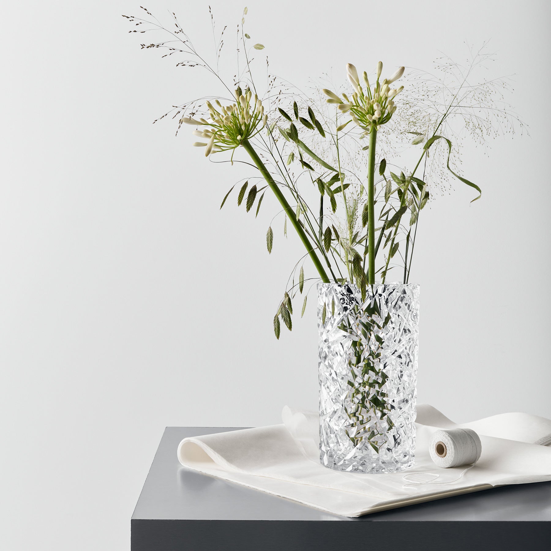 Clear glass vase with decorative pattern containing greenery on a white surface with a light gray background