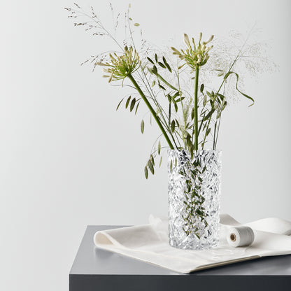 Clear glass vase with decorative pattern containing greenery on a white surface with a light gray background