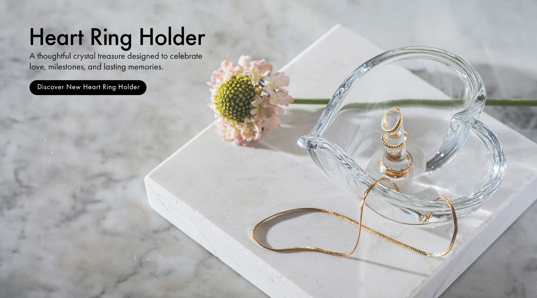 Crystal Heart Ring Holder sitting on marble surface holding gold chain and rings with flower stem next to it.