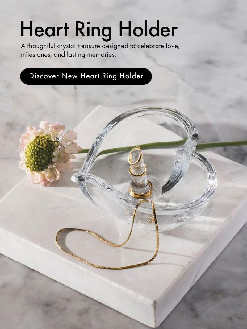 Crystal Heart Ring Holder sitting on marble surface holding gold chain and rings with flower stem next to it.