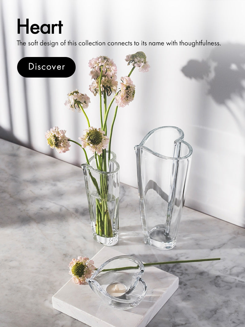 Heart-shaped glass vase with flowers on a marble surface with text describing Heart Collection.