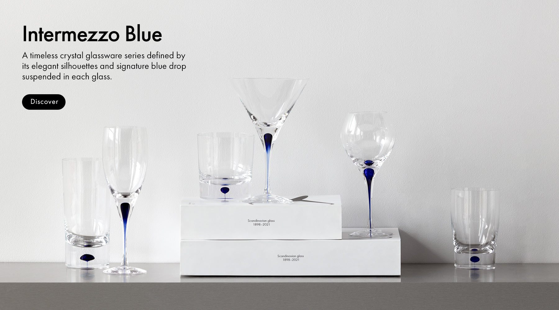 Intermezzo Blue collection glassware set on gray shelf with a white background with text describing the the collection.