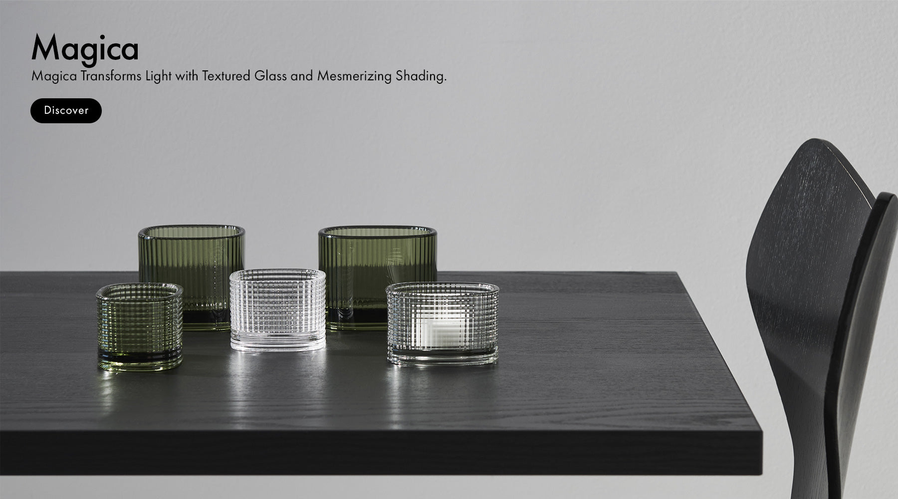 Magica Collection green votives and clear votives on a black wood table and text promoting transforming light and textured glass and mesmerizing shading.