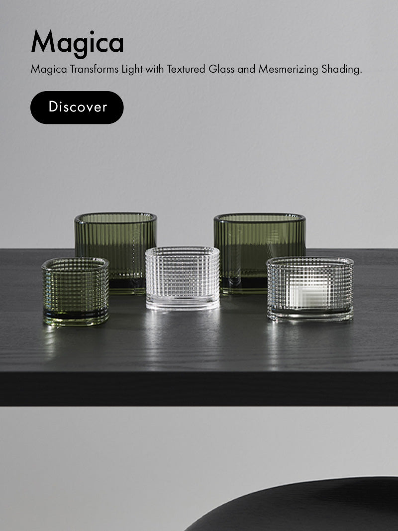 Magica Collection green votives and clear votives on a black wood table and text promoting transforming light and textured glass and mesmerizing shading.