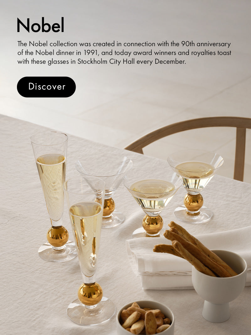 Mobile version of Nobel collection crystal drinkware on a  styled tabletop scene showing several clear champagne flutes with gold-colored bases, arranged on a white tablecloth beside a small bowl of cinnamon sticks and nuts. Text on the left reads 'Nobel' with a short description and a black 'Discover' button.