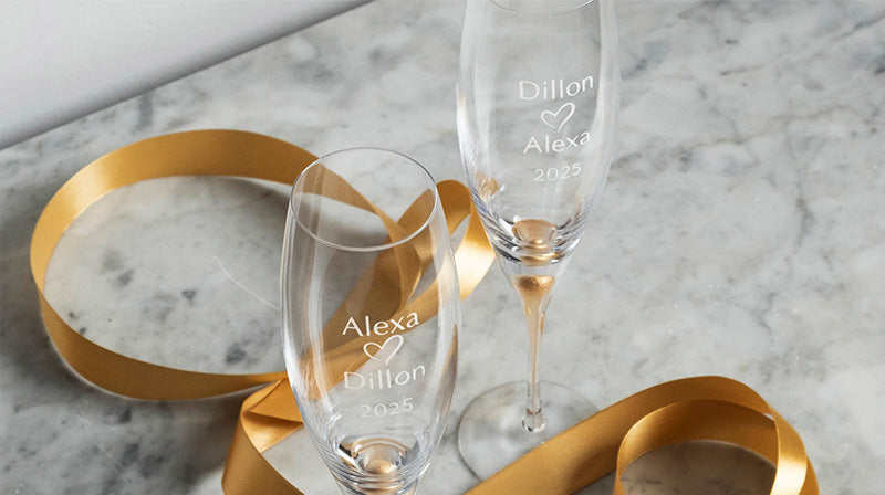 2 Engraved Intermezzo Gold champagne glasses with a gold ribbon on a light colored marble surface