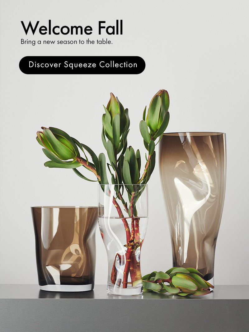 Three smoky amber glass table vases in different shapes, styled with green leaves and a water plant on a light gray background. Text on the left reads 'Welcome Fall' and 'Discover Squeeze Collection'.