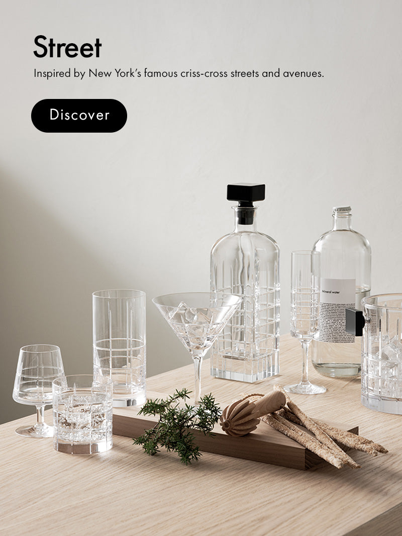 Street Collection with cut crystal grid pattern glasses, decanter, ice bucket and mineral water bottle sitting on wood surface with light background and text 'Street Inspired by New York's famous criss-cross streets and avenues.' and a Discover button.